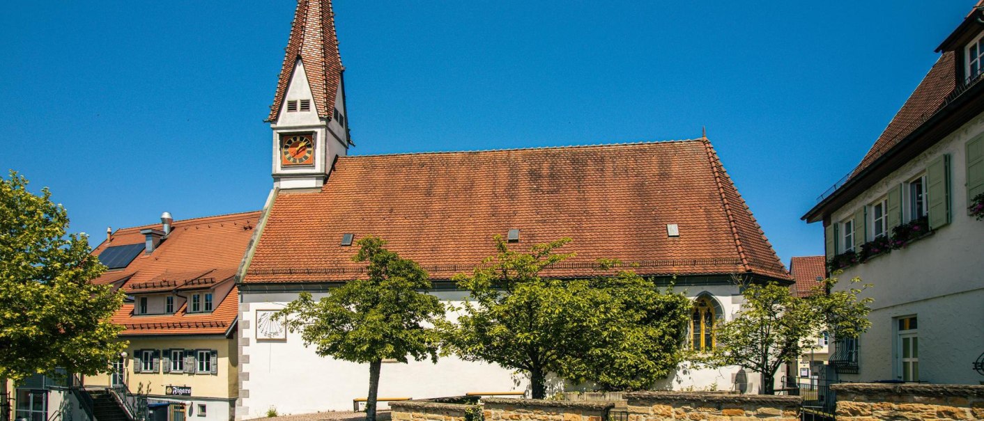 Historic church in Plochingen with red tiled roof and clock tower, surrounded by trees and blue sky., © Stuttgart-Marketing GmbH, Sarah Schmid Historic church in Plochingen with red tiled roof and clock tower, surrounded by trees and blue sky., © Stuttgart-Marketing GmbH, Sarah Schmid