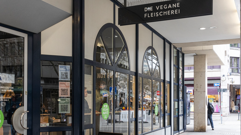 Entrance to the vegan butcher's shop in Stuttgart. The windows are large and there is a PETA Vegan Award sticker. Passers-by can be seen in the background., © Stuttgart-Marketing GmbH, Sarah Schmid Entrance to the vegan butcher's shop in Stuttgart. The windows are large and there is a PETA Vegan Award sticker. Passers-by can be seen in the background., © Stuttgart-Marketing GmbH, Sarah Schmid