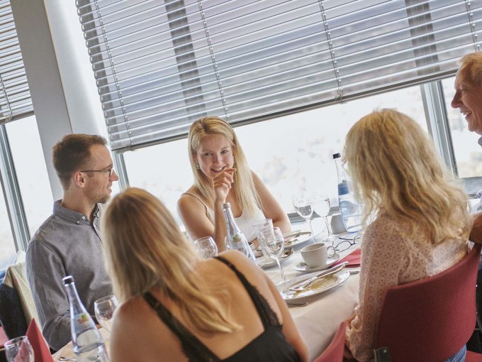 Eine Gruppe von Menschen sitzt an einem Tisch in einem Restaurant mit gro&szlig;en Fenstern. Sie unterhalten sich und genie&szlig;en Getr&auml;nke., &copy; SWR Media Services GmbH / Fernsehturm Stuttgart