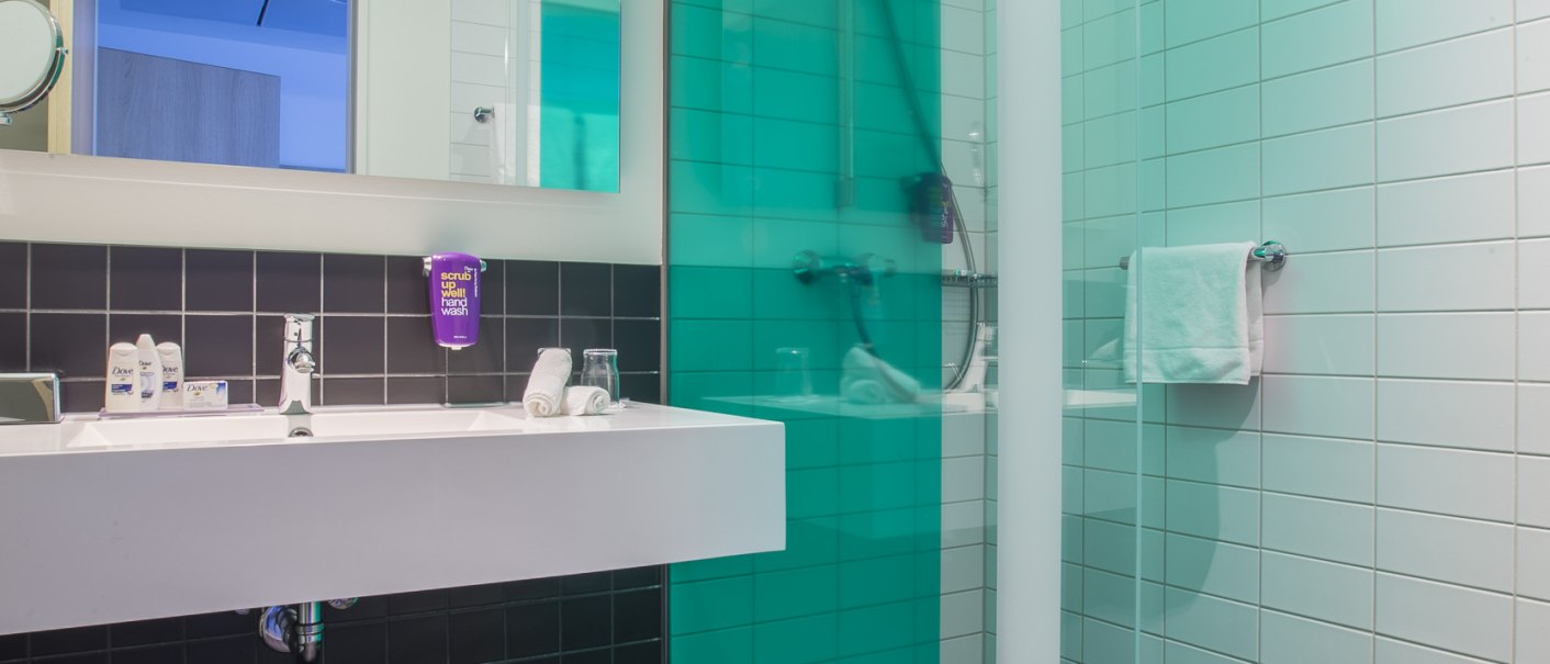 Modernes Badezimmer mit Glasdusche, weißem Waschbecken und großem Spiegel. Schwarze und weiße Fliesen dominieren das Design., © Park Inn by Radisson Stuttgart