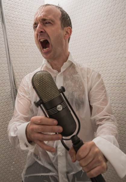 Ein Mann in einem nassen Hemd singt leidenschaftlich in der Dusche und h&auml;lt ein Mikrofon. Die Szene wirkt energiegeladen und emotional., &copy; Rosenau Kultur e.V.