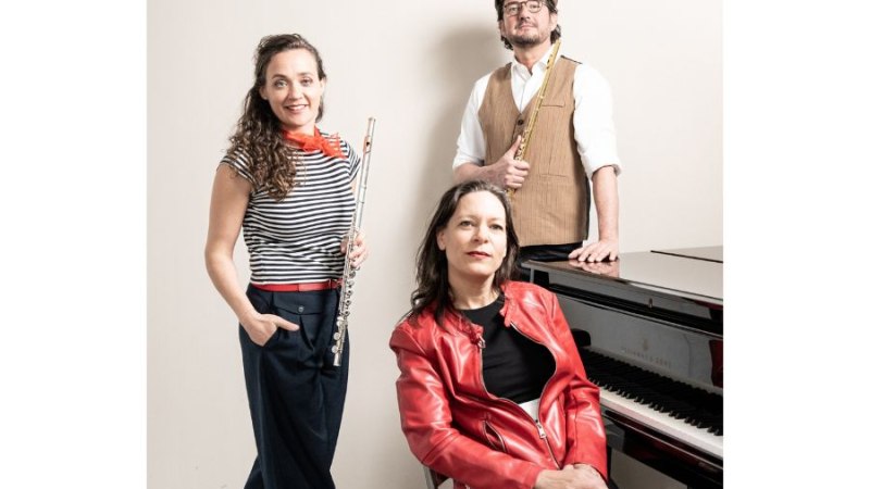 Drei Musiker posieren vor einem Klavier. Zwei halten Flöten, eine Person sitzt am Klavier. Sie tragen stilvolle, farbenfrohe Kleidung., © Trio Funkenflug Drei Musiker posieren vor einem Klavier. Zwei halten Flöten, eine Person sitzt am Klavier. Sie tragen stilvolle, farbenfrohe Kleidung., © Trio Funkenflug