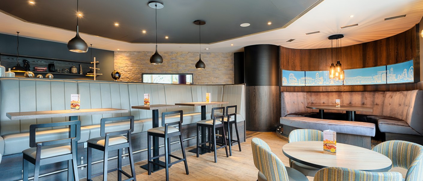 Moderner Fr&uuml;hst&uuml;cksbereich mit stilvollen Sitzgelegenheiten, H&auml;ngelampen und Wandkunst. Holzboden und gem&uuml;tliche Atmosph&auml;re., &copy; Premier Inn Germany