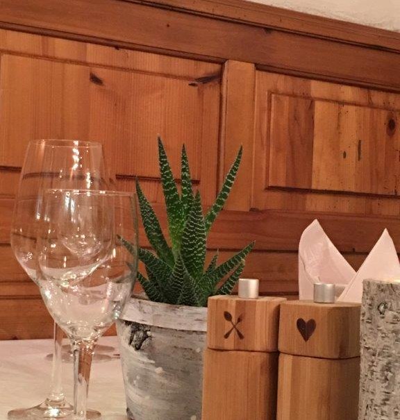 Tisch in einem Restaurant mit Weingläsern, einer kleinen Pflanze und Holzgewürzstreuern vor einer Holzwand., © TOMAS