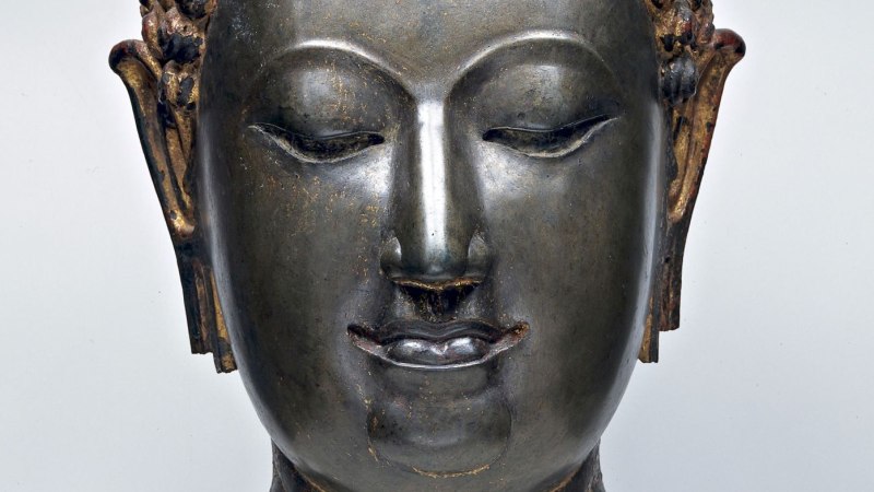 Nahaufnahme eines Buddha-Kopfes aus Metall, 14. Jh., Thailand. Der Buddha hat geschlossene Augen und ein sanftes Lächeln., © Linden-Museum Stuttgart, Foto Anatol Dreyer Nahaufnahme eines Buddha-Kopfes aus Metall, 14. Jh., Thailand. Der Buddha hat geschlossene Augen und ein sanftes Lächeln., © Linden-Museum Stuttgart, Foto Anatol Dreyer