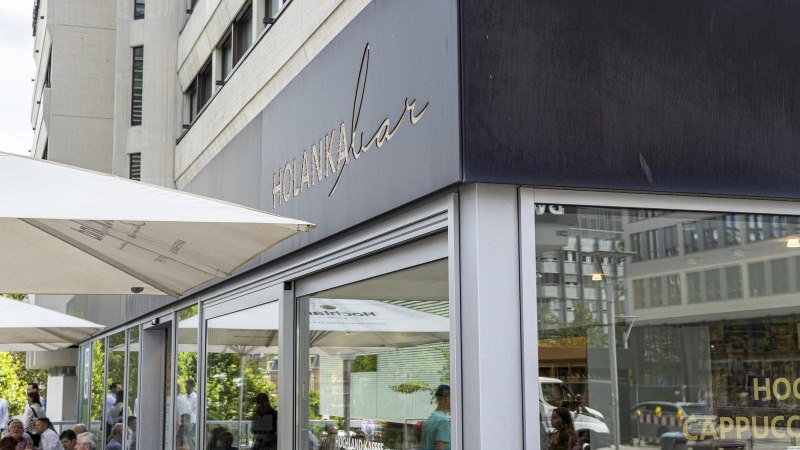 Außenansicht der Holanka Bar mit großen Sonnenschirmen. Menschen sitzen und stehen im Außenbereich. Moderne Gebäude im Hintergrund., © SMG, Sarah Schmid Außenansicht der Holanka Bar mit großen Sonnenschirmen. Menschen sitzen und stehen im Außenbereich. Moderne Gebäude im Hintergrund., © SMG, Sarah Schmid