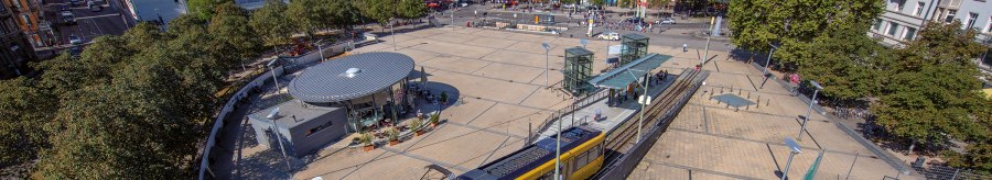 Aerial view of Marienplatz in Stuttgart. A yellow streetcar passes by, surrounded by trees and buildings. The square is lively and sunny., &copy; Stuttgart-Marketing GmbH