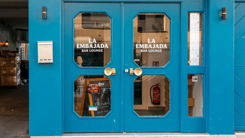 Gro&szlig;e Doppelt&uuml;r in leuchtendem Blau mit Glaseins&auml;tzen, auf denen "La Embajada Bar Lounge" in wei&szlig;en Lettern geschrieben steht., &copy; SMG Stuttgart Marketing GmbH - Sarah Schmid