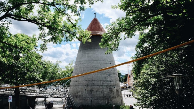 Ein Winkelturm mit rotem Dach umgeben von Bäumen, unter einem blauen Himmel. Menschen gehen auf einem gepflasterten Weg., © tmbw, Susi Maier