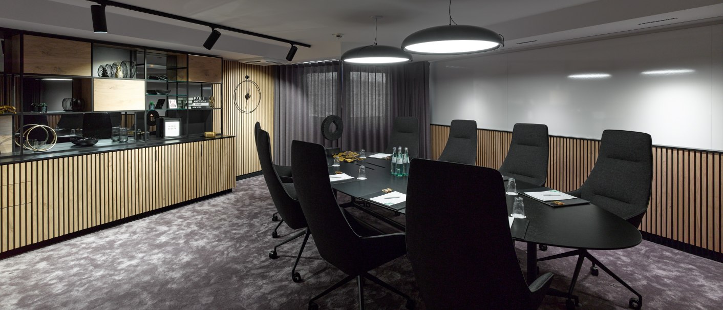 Modern conference room with oval table, black chairs, wood paneling and shelves. Two large lamps hang from the ceiling., © Holiday Inn Stuttgart Modern conference room with oval table, black chairs, wood paneling and shelves. Two large lamps hang from the ceiling., © Holiday Inn Stuttgart