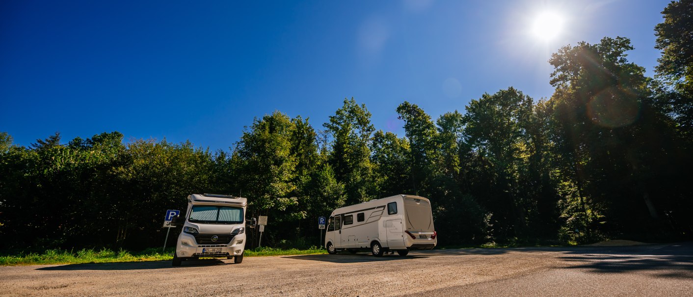 Zwei Wohnmobile stehen auf einem Parkplatz im Stadtpark Welzheim. Der Himmel ist klar und die Sonne scheint hell. Bäume umgeben den Platz., © Stuttgart-Marketing GmbH, Thomas Niedermüller