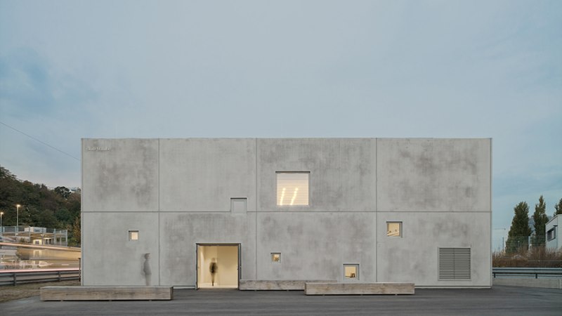 Ein modernes Geb&auml;ude mit Betonfassade und kleinen Fenstern. Die minimalistische Architektur hebt sich gegen den blauen Himmel ab., &copy; club traube