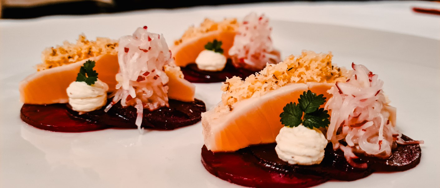 Gourmetgericht mit eingelegter Forelle, Rote Bete, Sahne und Kräutern auf einem weißen Teller kunstvoll angerichtet., © Hupperts