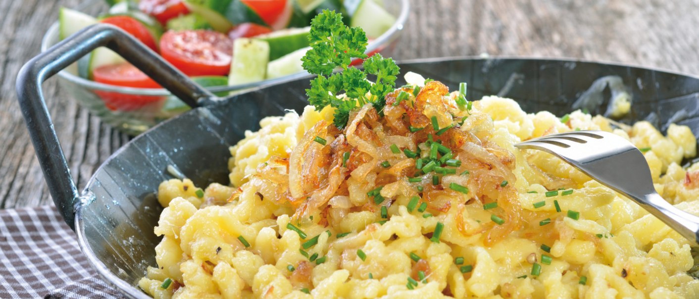 Cheese spaetzle with fried onions and chives in a pan, served with a fresh salad of tomatoes and cucumber., © kab-vision - Fotolia Cheese spaetzle with fried onions and chives in a pan, served with a fresh salad of tomatoes and cucumber., © kab-vision - Fotolia