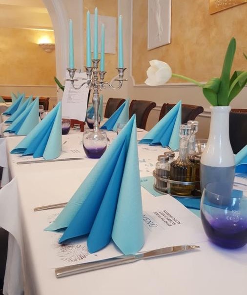 Ein elegant gedeckter Tisch in einem Restaurant mit blauen Servietten, Kerzenleuchter und weißen Tulpen. Die Atmosphäre ist stilvoll und einladend., © Hotel Engelhof
