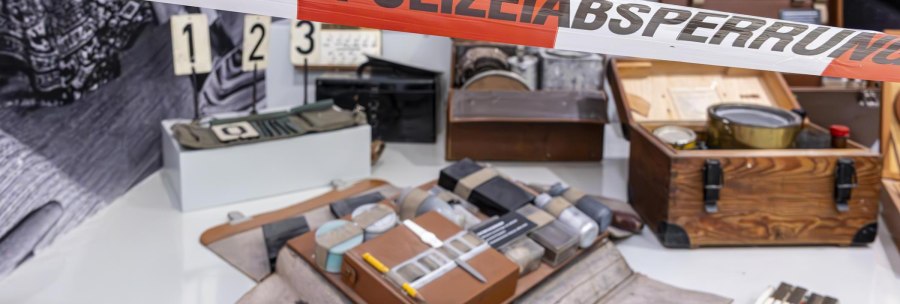 Ausstellungsstücke im Polizeimuseum Stuttgart, darunter alte Polizeiausrüstung und Beweismaterial, hinter einem Absperrband mit der Aufschrift 'POLIZEIABSPERRUNG'., © Stuttgart-Marketing GmbH, Sarah Schmid