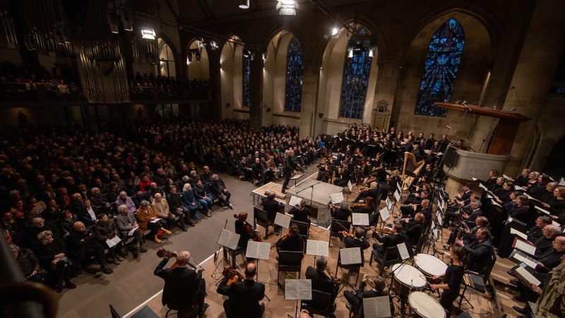 Ein Orchester und Chor führen in einer Kirche vor einem großen Publikum auf. Die Kirche hat hohe Fenster und eine Orgel., © www.hassfoto.de