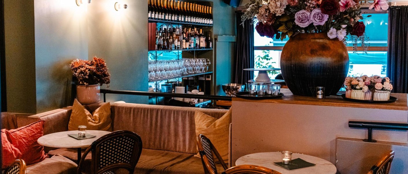 Gemütliches Café mit Sofas, runden Tischen und Blumenarrangements. Im Hintergrund Weinflaschen und Gläserregale., © Stuttgart Marketing GmbH - Sarah Schmid