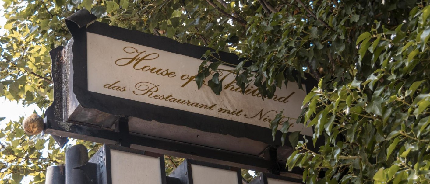 Ein Schild mit der Aufschrift 'House of Thailand, das Restaurant mit Niveau', umgeben von gr&uuml;nen Bl&auml;ttern., &copy; Stuttgart Marketing GmbH, Sarah Schmid