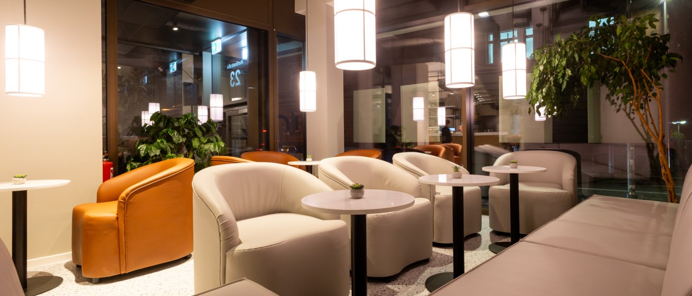 Moderne Lounge mit weißen und braunen Sesseln, kleinen runden Tischen und hängenden Lampen. Große Fenster und Pflanzen schaffen eine gemütliche Atmosphäre., © GINN Apartments Esslingen Moderne Lounge mit weißen und braunen Sesseln, kleinen runden Tischen und hängenden Lampen. Große Fenster und Pflanzen schaffen eine gemütliche Atmosphäre., © GINN Apartments Esslingen