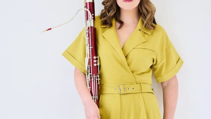 Eine Person in einem gelben Overall hält ein Fagott vor einem weißen Hintergrund. Sie hat schulterlanges Haar und schaut direkt in die Kamera., © Klassische Philharmonie Bonn e.V. Eine Person in einem gelben Overall hält ein Fagott vor einem weißen Hintergrund. Sie hat schulterlanges Haar und schaut direkt in die Kamera., © Klassische Philharmonie Bonn e.V.