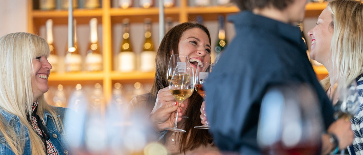 Four people clink glasses of wine in a wine shop and laugh. Wine bottles can be seen in the background., © Stuttgart-Marketing GmbH, Thomas Niedermüller