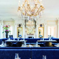 Elegantes Restaurant mit Kronleuchter, blauen Sitzb&auml;nken und wei&szlig;en S&auml;ulen. Blumenarrangements und gedeckte Tische schaffen eine luxuri&ouml;se Atmosph&auml;re., &copy; Speisemeisterei