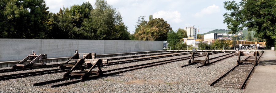 Gedenkst&auml;tte mit stillgelegten Bahngleisen, umgeben von B&auml;umen und einer Mauer. Ein ruhiger Ort des Erinnerns., &copy; Foto-Kunst Andreas Keller