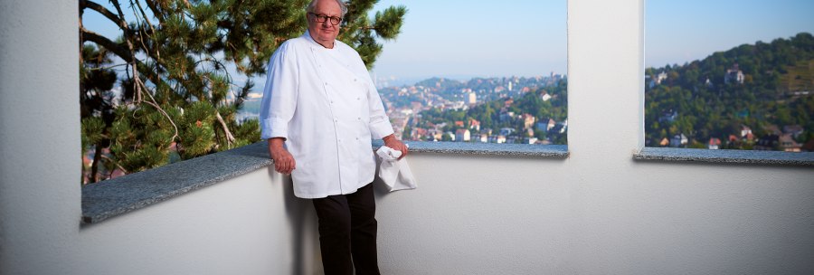 A cook in a white uniform leans against a balcony parapet. A cityscape can be seen in the background., &copy; SMG, Jean-Claude Winkler