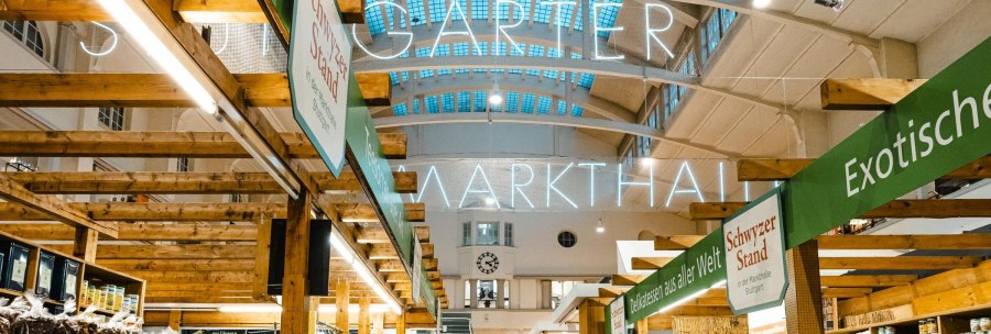 Interior view of the Stuttgart market hall with wooden stalls, illuminated signage and various delicatessen stalls., © by Canto