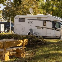 Wohnmobile auf einem sonnigen Campingplatz, umgeben von B&auml;umen. Im Vordergrund steht ein Holztisch mit B&auml;nken., &copy; Stuttgart-Marketing GmbH, Sarah Schmid