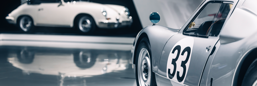 Two classic cars in an exhibition. A white convertible with police lights and a silver car with the number 33 in the foreground., © Porsche AG Two classic cars in an exhibition. A white convertible with police lights and a silver car with the number 33 in the foreground., © Porsche AG