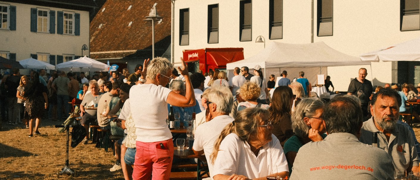 People are sitting and standing at an outdoor wine festival. There are tables, marquees and a relaxed atmosphere., &copy; MyDegerloch