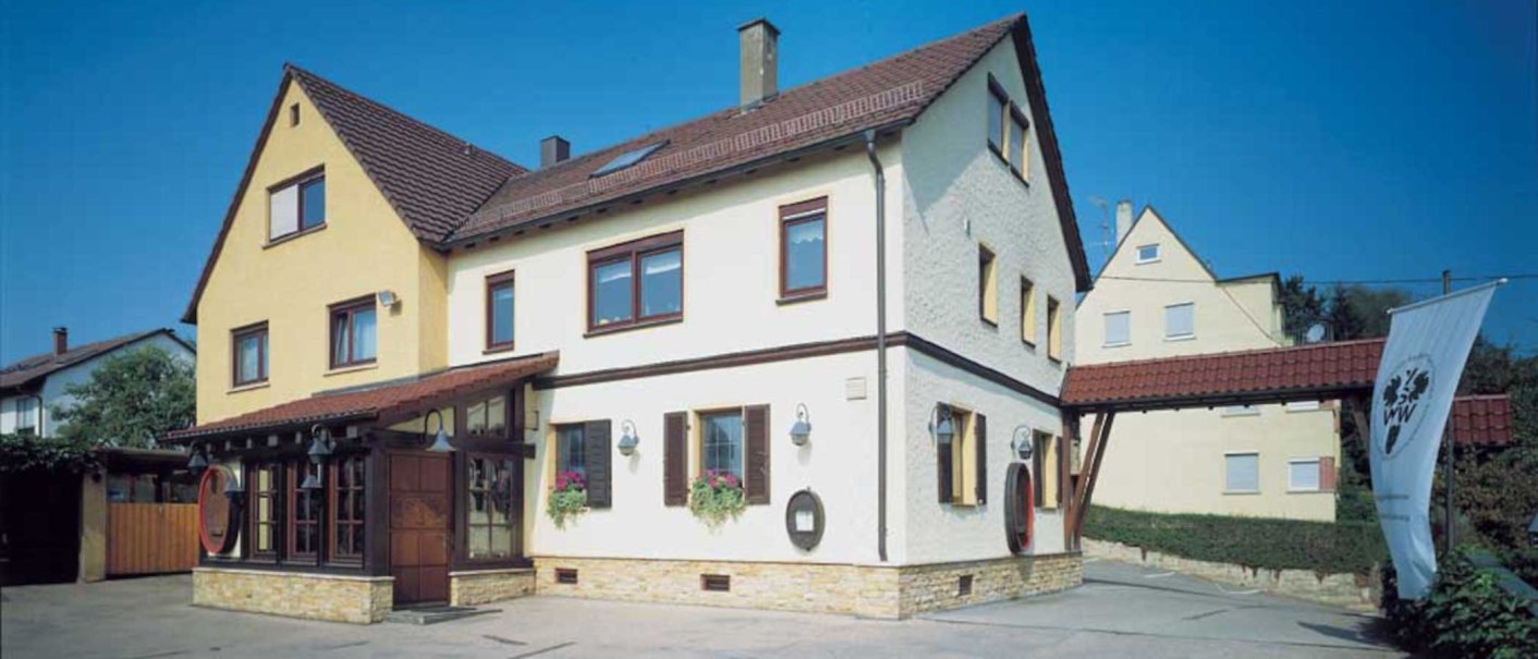Zweistöckiges Gebäude mit gelber und weißer Fassade, roten Dachziegeln. Ein VdW-Banner steht davor. Klare, blaue Himmel im Hintergrund., © Weinstube Jägerhof