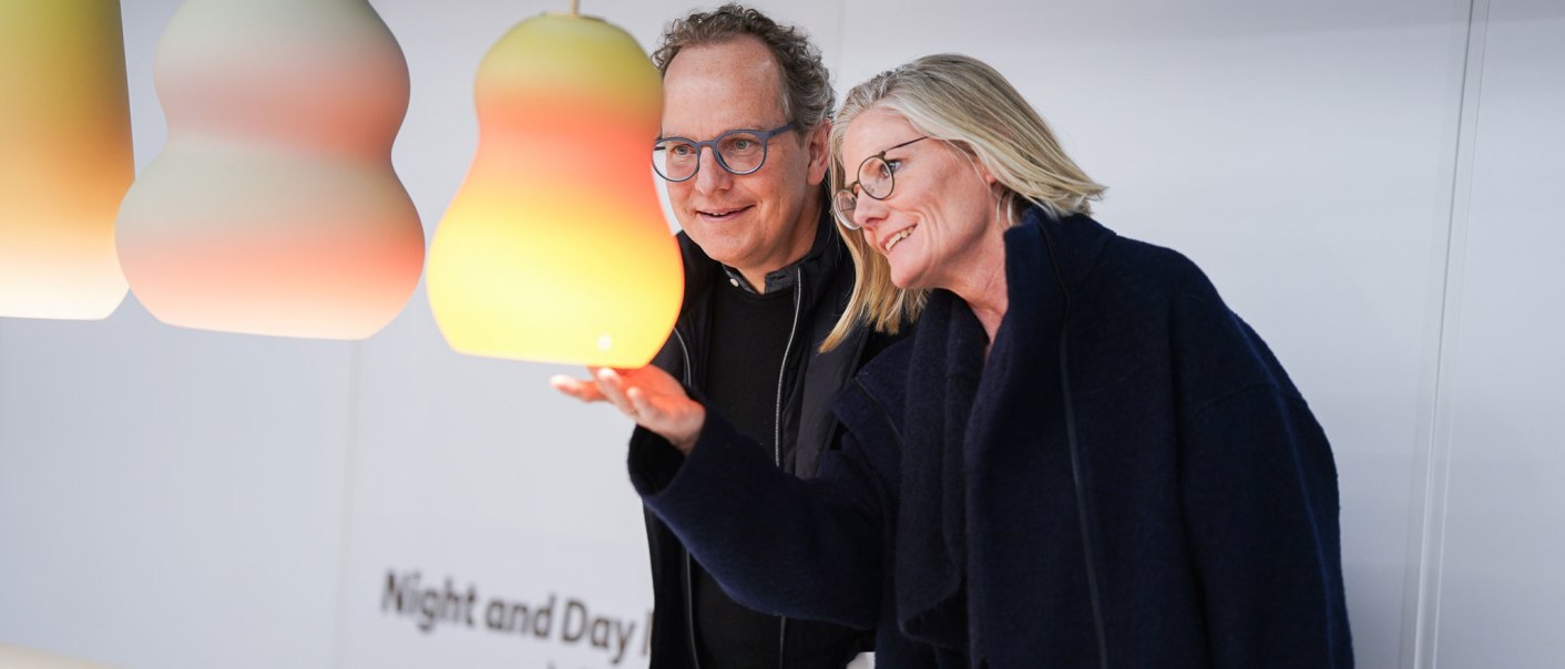 Zwei Personen betrachten bunte, birnenf&ouml;rmige Lampen auf der BLICKFANG Stuttgart. Die Lampen leuchten in sanften Farbverl&auml;ufen., &copy; BLICKFANG GmbH