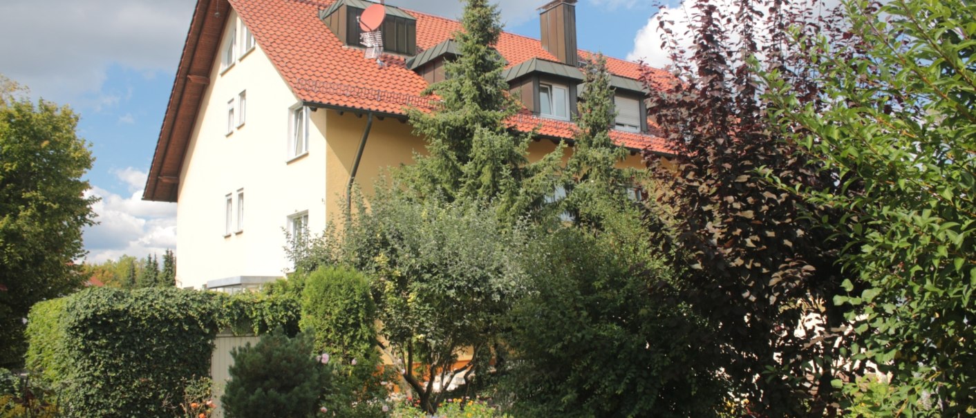 Ein Hotel mit rotem Dach und gelber Fassade, umgeben von einem üppigen Garten mit Bäumen und Sträuchern., © TOMAS Ein Hotel mit rotem Dach und gelber Fassade, umgeben von einem üppigen Garten mit Bäumen und Sträuchern., © TOMAS
