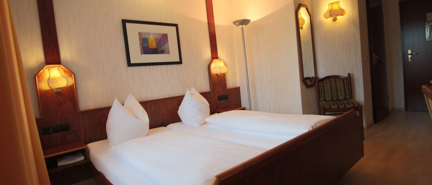 Cozy double room with wooden furniture, large bed, wall lamps and picture on the wall. Bright, warm lighting and a chair in the corner., © TOMAS Cozy double room with wooden furniture, large bed, wall lamps and picture on the wall. Bright, warm lighting and a chair in the corner., © TOMAS