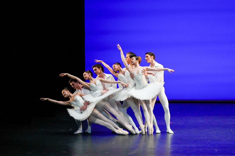 Balletttänzer in weißen Kostümen posieren synchron auf einer Bühne vor einem blauen Hintergrund. Elegante und harmonische Choreografie., © Württembergische Staatstheater Stuttgart