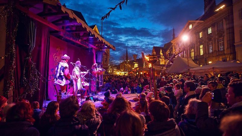 Menschenmenge genießt eine Aufführung auf dem Esslinger Mittelaltermarkt & Weihnachtsmarkt bei Abenddämmerung. Stände und Lichter im Hintergrund., © Esslinger Markt & Event GmbH (EME) Menschenmenge genießt eine Aufführung auf dem Esslinger Mittelaltermarkt & Weihnachtsmarkt bei Abenddämmerung. Stände und Lichter im Hintergrund., © Esslinger Markt & Event GmbH (EME)