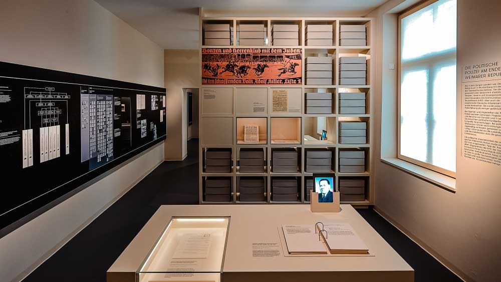 Ein Ausstellungsraum mit Regalen voller Archivboxen, Dokumenten auf einem Tisch und Informationstafeln an den Wänden., © Haus der Geschichte Baden-Württemberg Ein Ausstellungsraum mit Regalen voller Archivboxen, Dokumenten auf einem Tisch und Informationstafeln an den Wänden., © Haus der Geschichte Baden-Württemberg