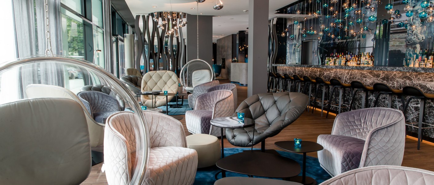 Modern lobby with elegant armchairs, round tables and a stylish bar. Hanging lamps and large windows create an inviting atmosphere., &copy; Motel One Stuttgart-Bad Cannstatt