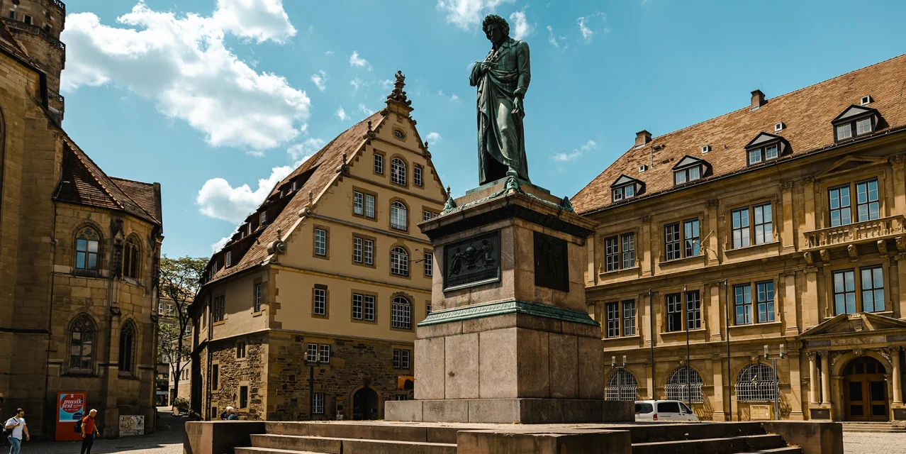 Schillerdenkmal auf dem Platz, umgeben von historischen Gebäuden unter blauem Himmel., © SMG, Sarah Schmid Schillerdenkmal auf dem Platz, umgeben von historischen Gebäuden unter blauem Himmel., © SMG, Sarah Schmid