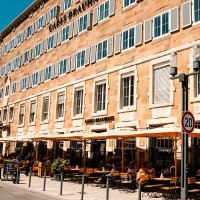Carls Brauhaus mit gelbem Gebäude, vielen Fenstern und Außenterrasse mit Sonnenschirmen und Sitzplätzen. Menschen genießen das sonnige Wetter., © Stuttgart Marketing GmbH, Sarah Schmid