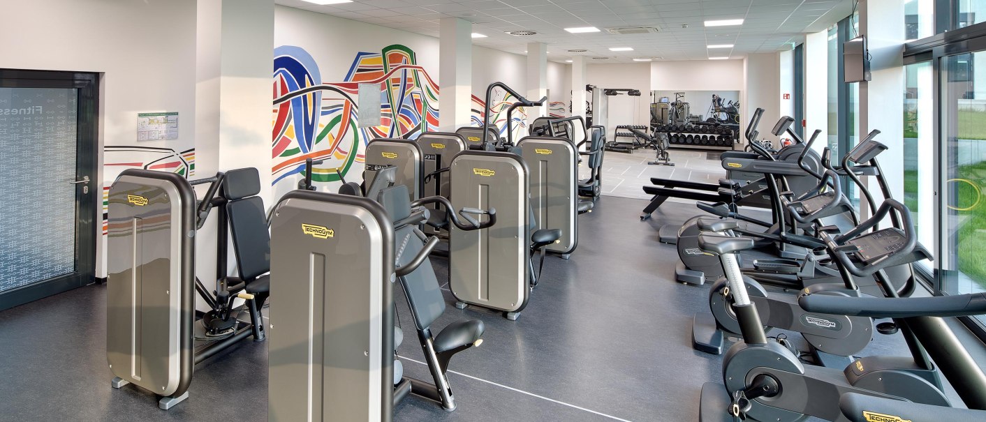Modern fitness studio with various training equipment, colorful wall art and large windows for plenty of natural light., &copy; Hotel am Remspark