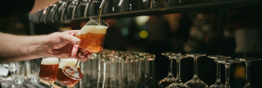A bartender draws beer from a tap into a glass. More glasses are ready. The scene takes place at a bar., © Kraftpaule GmbH A bartender draws beer from a tap into a glass. More glasses are ready. The scene takes place at a bar., © Kraftpaule GmbH