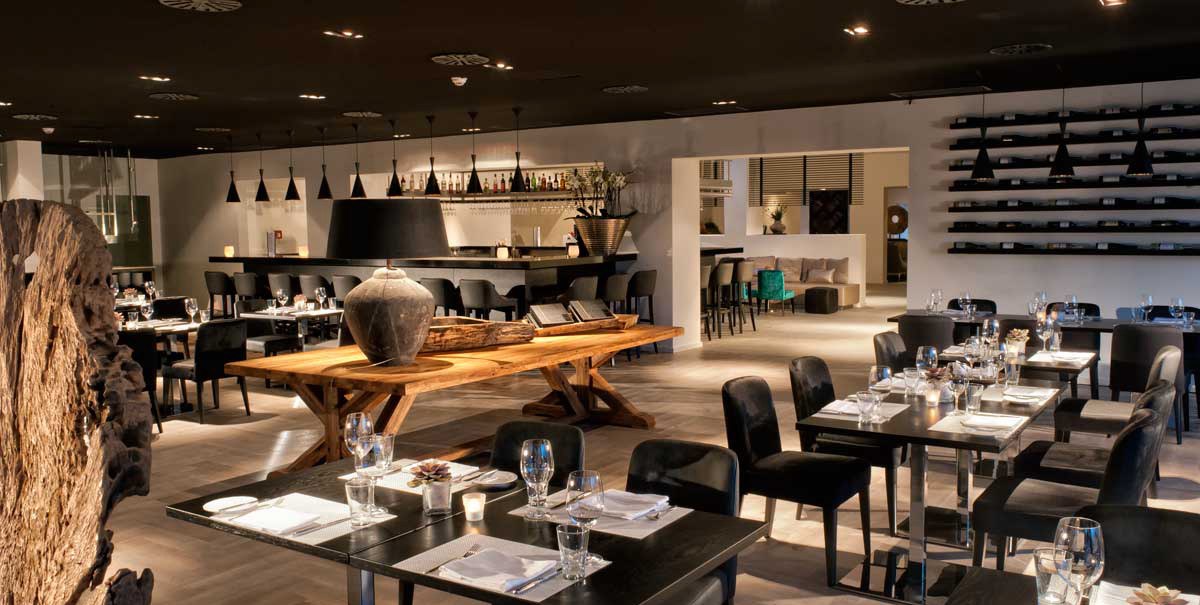 Modern restaurant with elegant furnishings, laid tables and stylish lighting. A bar with bottle rack in the background., &copy; Wyndham Stuttgart Airport Messe