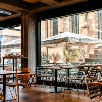 Modernes Caf&eacute; mit Holzm&ouml;beln, gro&szlig;en Fenstern und Blick auf eine Terrasse mit "Citizen Long"-Sonnenschirmen., &copy; SMG Stuttgart Marketing GmbH - Sarah Schmid