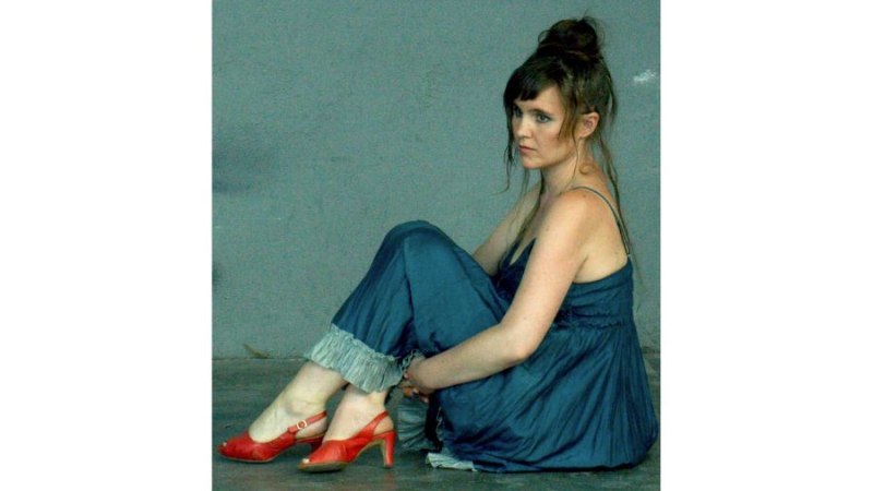 Frau in blauem Kleid und roten Schuhen sitzt nachdenklich auf dem Boden vor einer grauen Wand., © Fotocredit Theater La Lune Stuttgart Frau in blauem Kleid und roten Schuhen sitzt nachdenklich auf dem Boden vor einer grauen Wand., © Fotocredit Theater La Lune Stuttgart