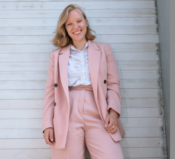 Eine l&auml;chelnde Person in einem rosa Anzug steht vor einer wei&szlig;en Wand. Sie tr&auml;gt ein wei&szlig;es Hemd und hat blonde Haare., &copy; Mafalda Rakoš