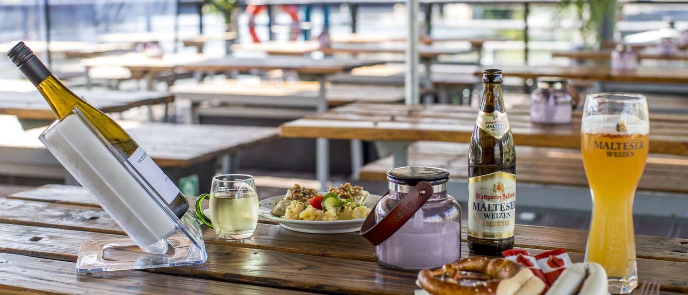Beer garden with wooden tables, white wine, Malteser wheat beer, white sausages, pretzels and potato salad. A river can be seen in the background., © all copyrights are reserved by maks richter